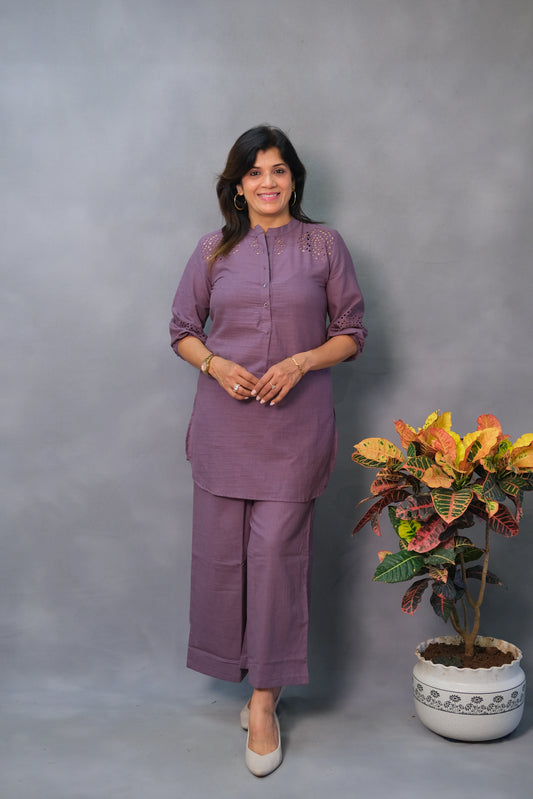 Woman in a purple outfit standing next to a potted plant against a gray background