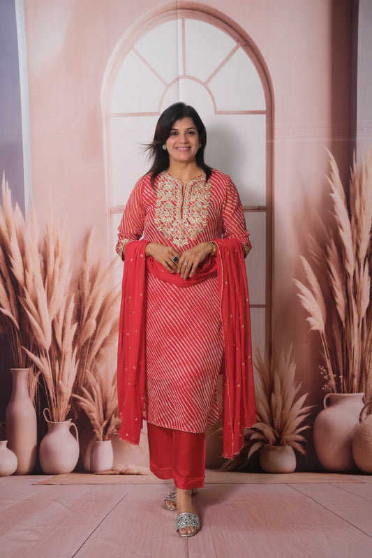 Woman in a red traditional outfit standing in front of decorative archway and plants.