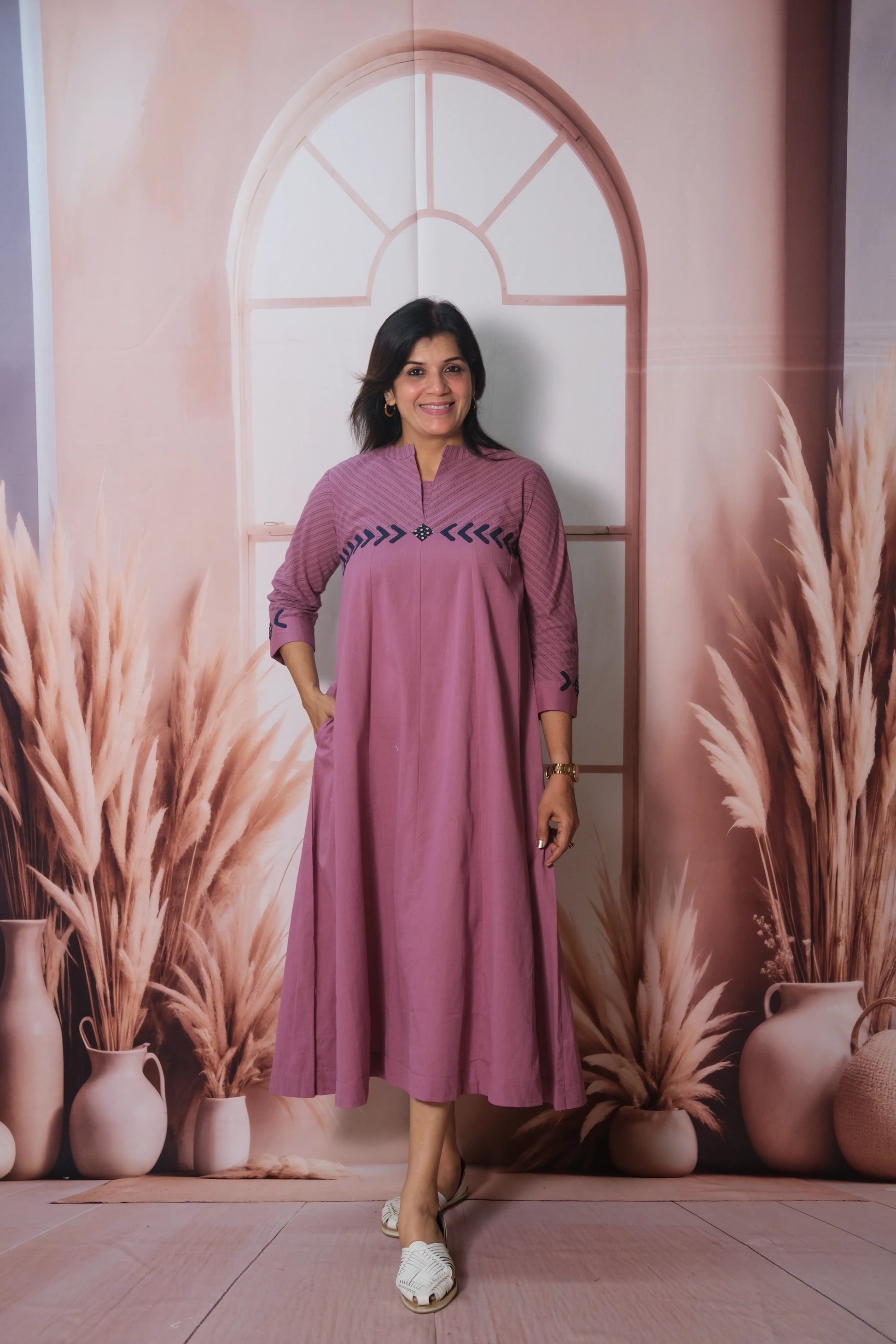 Woman in a pink dress standing in front of a decorative wall with plants and vases.