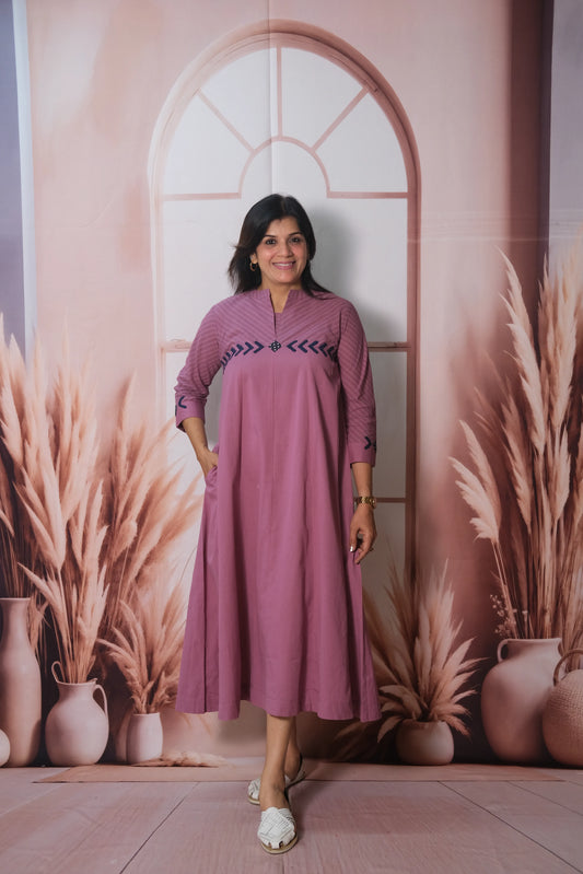 Woman in a pink dress standing in front of a decorative wall with plants and vases.
