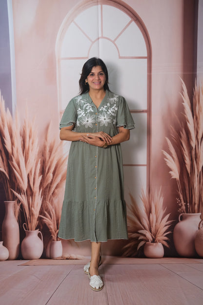 Woman in a green dress standing in front of a decorative wall with arches and plants.