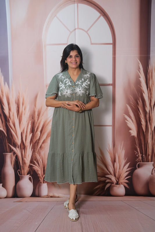 Woman in a green dress standing in front of a decorative wall with arches and plants.