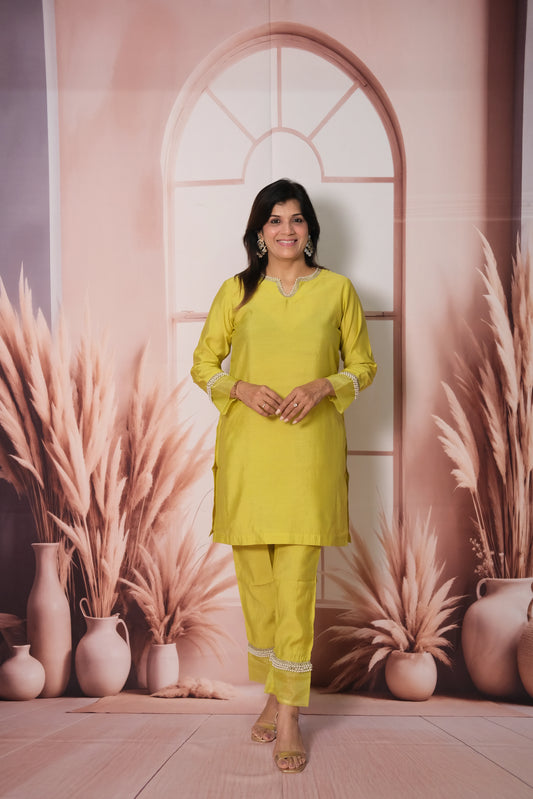 Woman in a bright yellow outfit standing in front of a decorative wall with plants and vases.