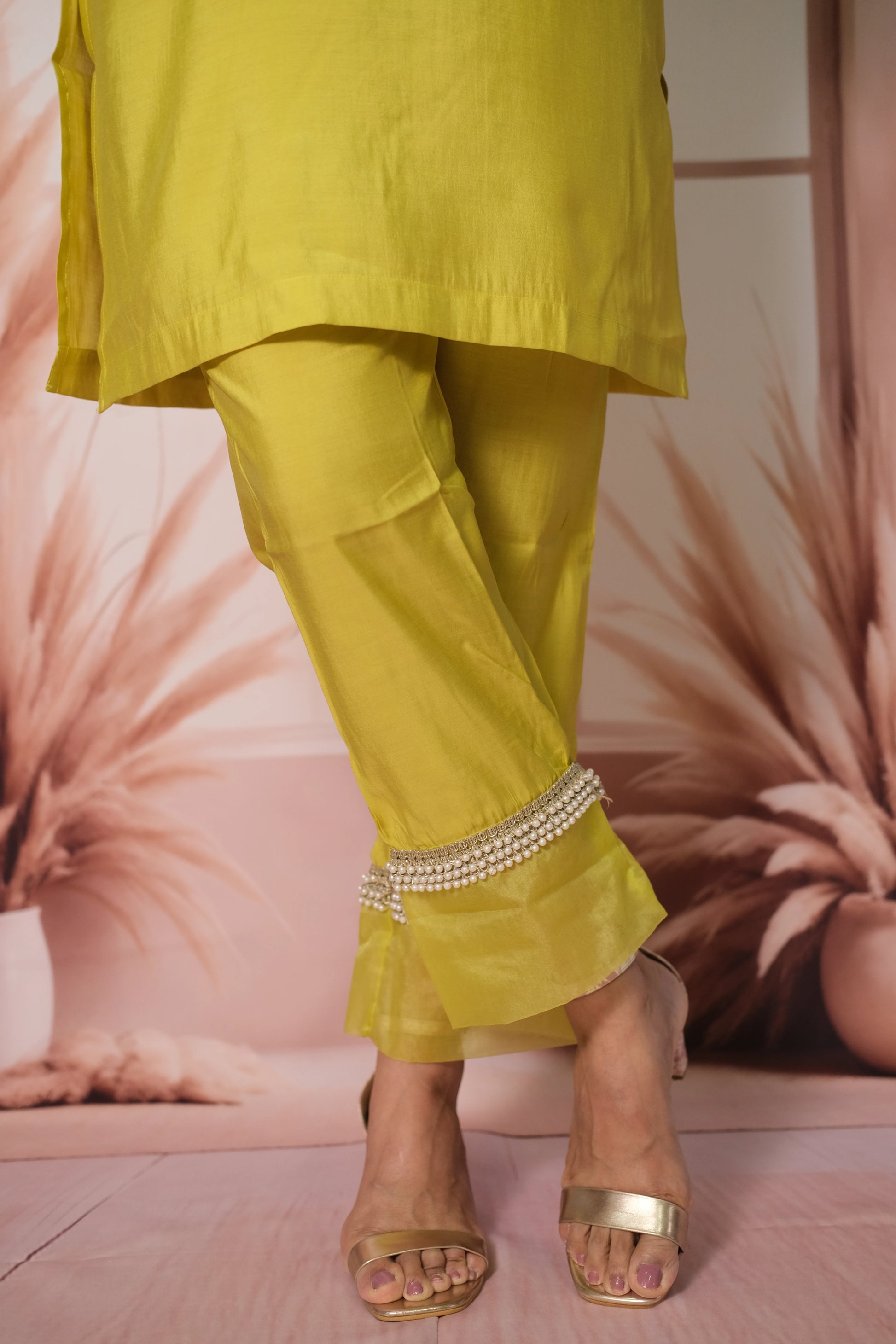 Person wearing a bright yellow outfit with embellished pants against a pink floral background