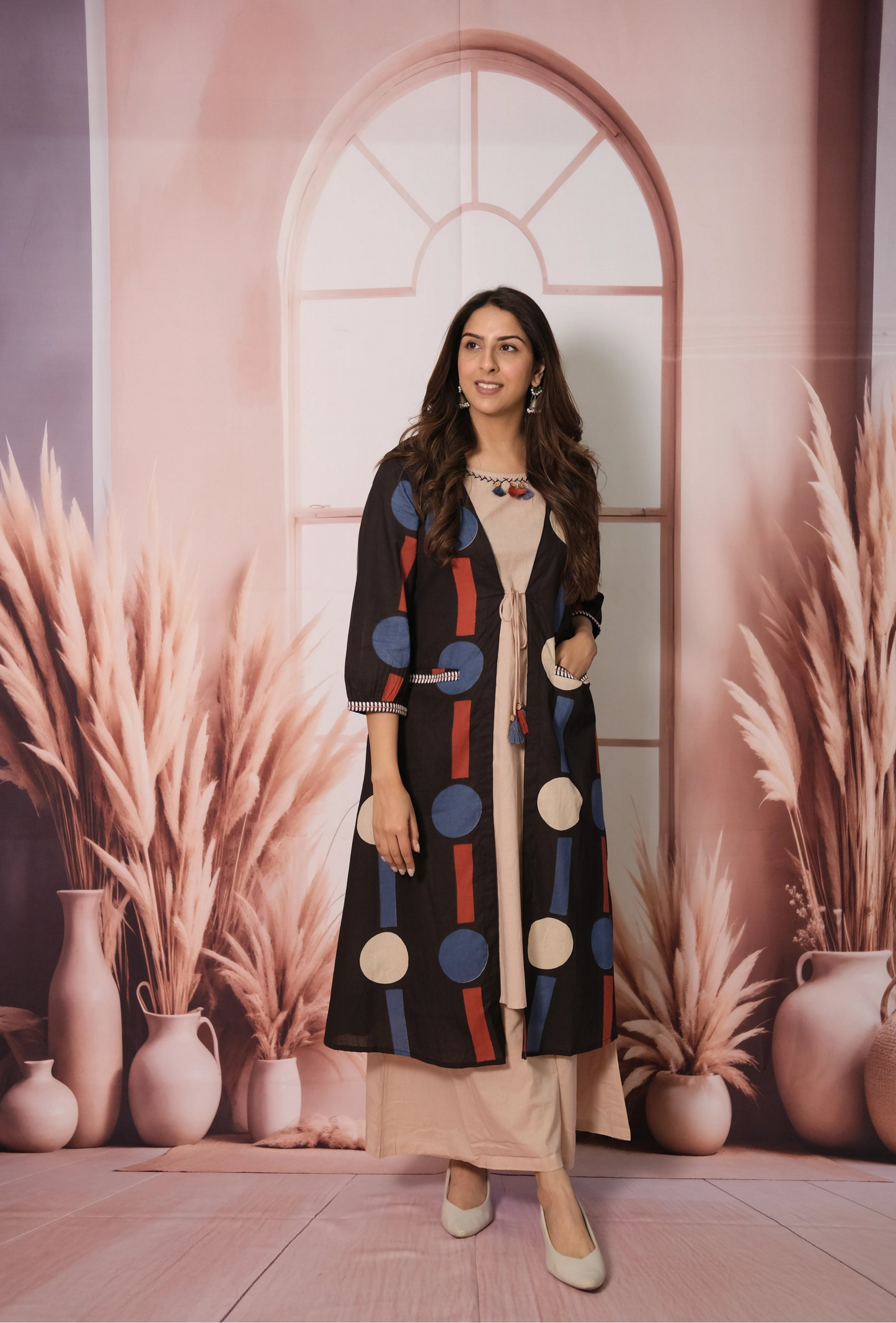 Woman in a colorful outfit standing in front of a decorative wall with vases and plants.