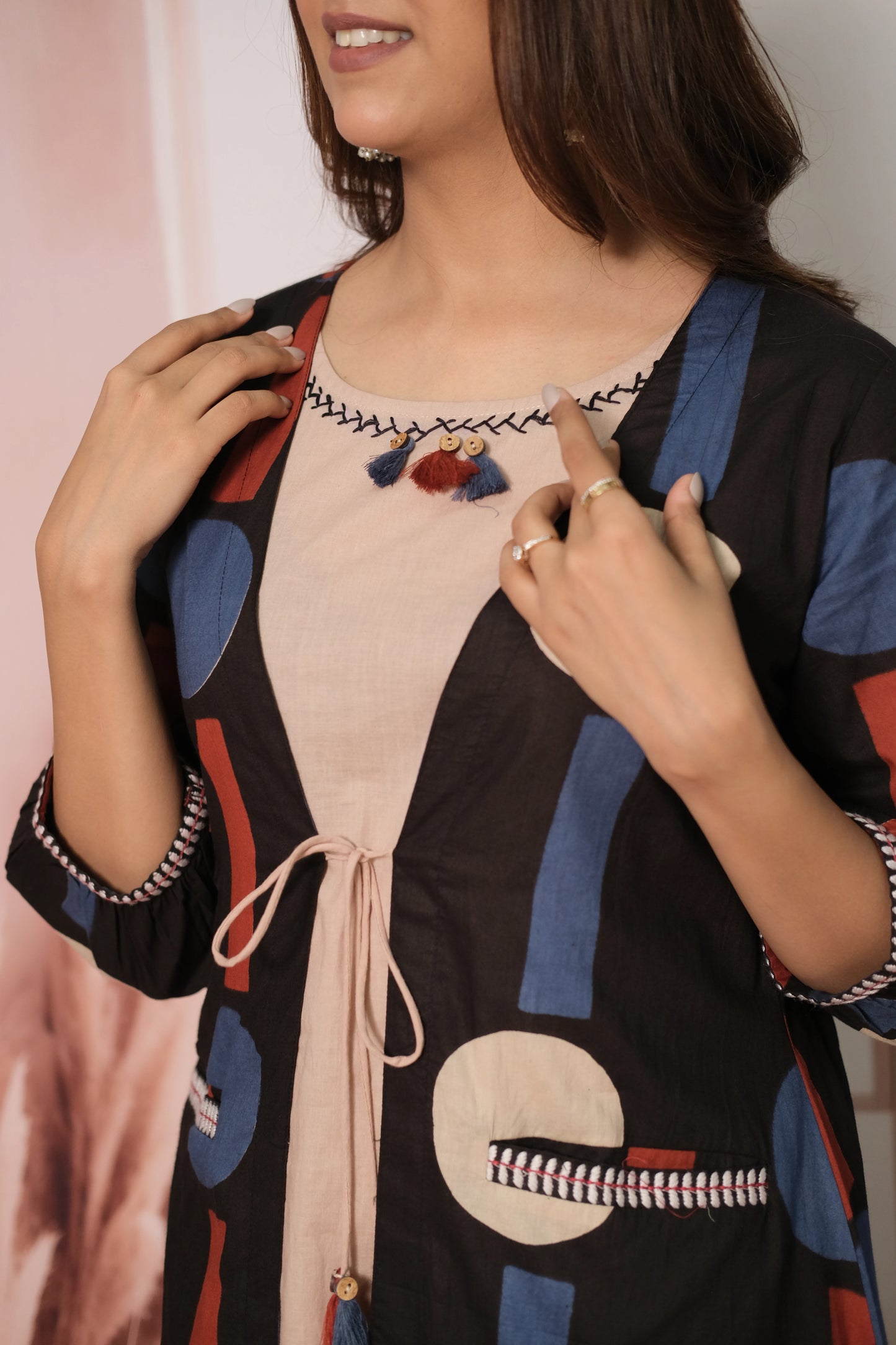 Woman wearing a black cardigan with colorful patterns over a pink top.