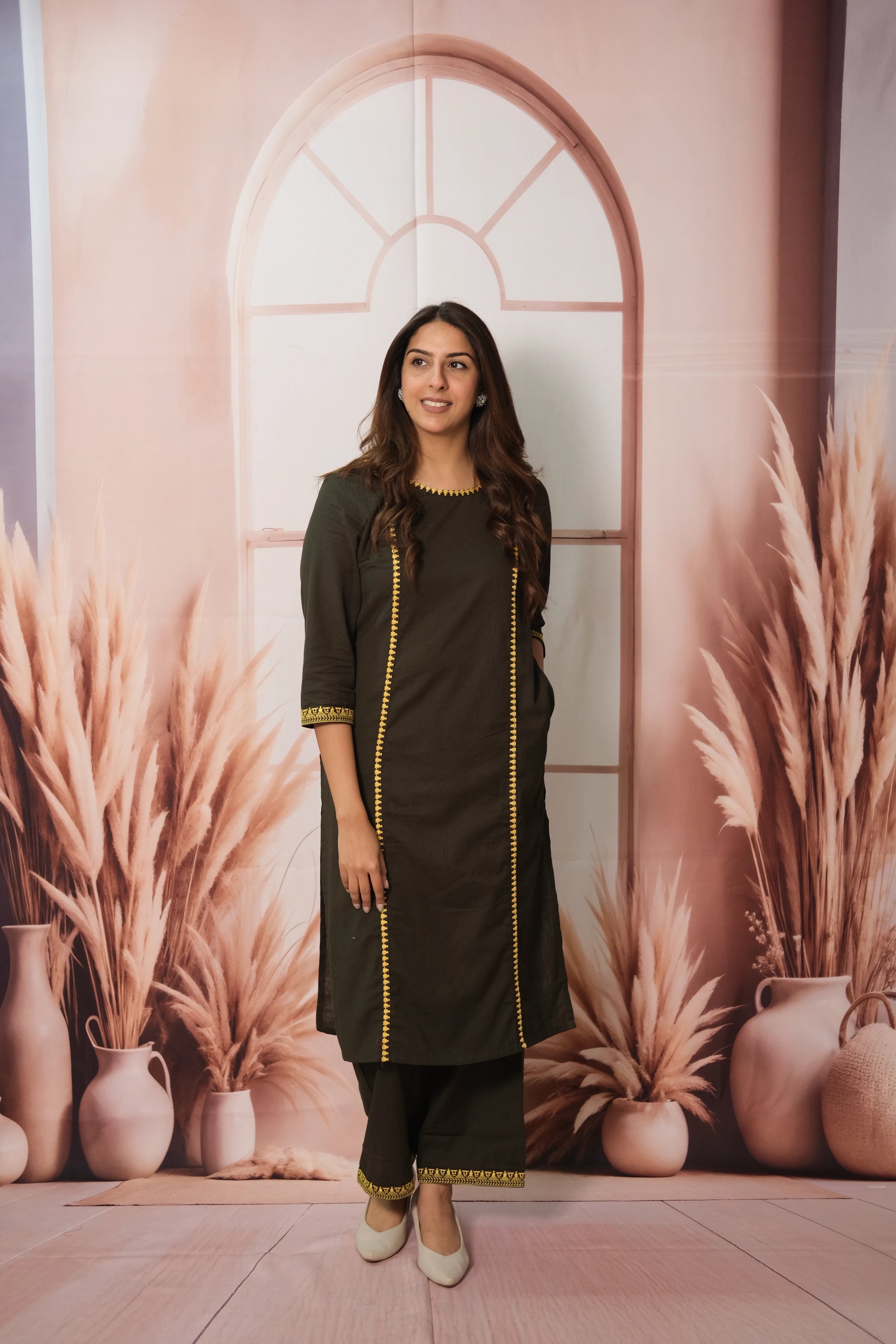 Woman in a green dress standing in front of a decorative wall with plants and vases.