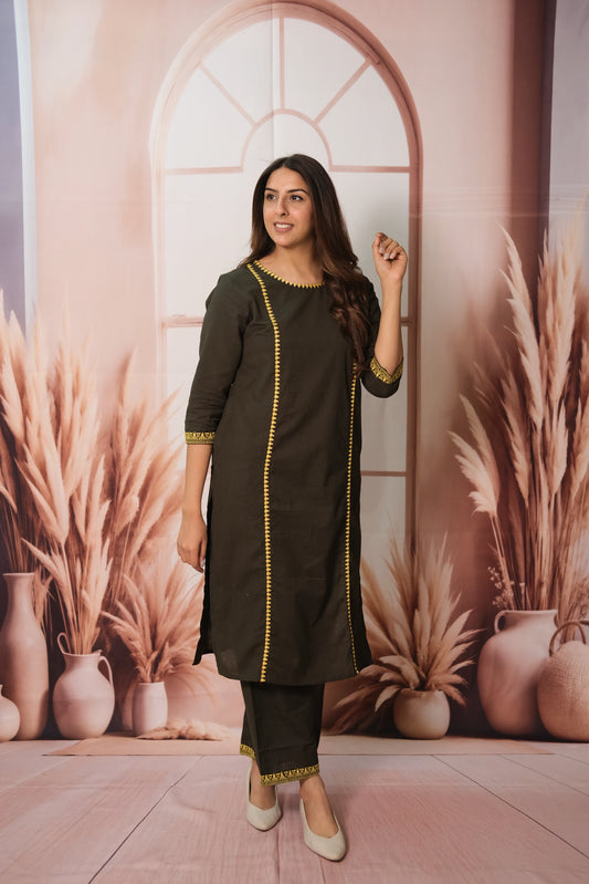 Woman in a green traditional outfit standing in front of a decorative wall with plants and vases.