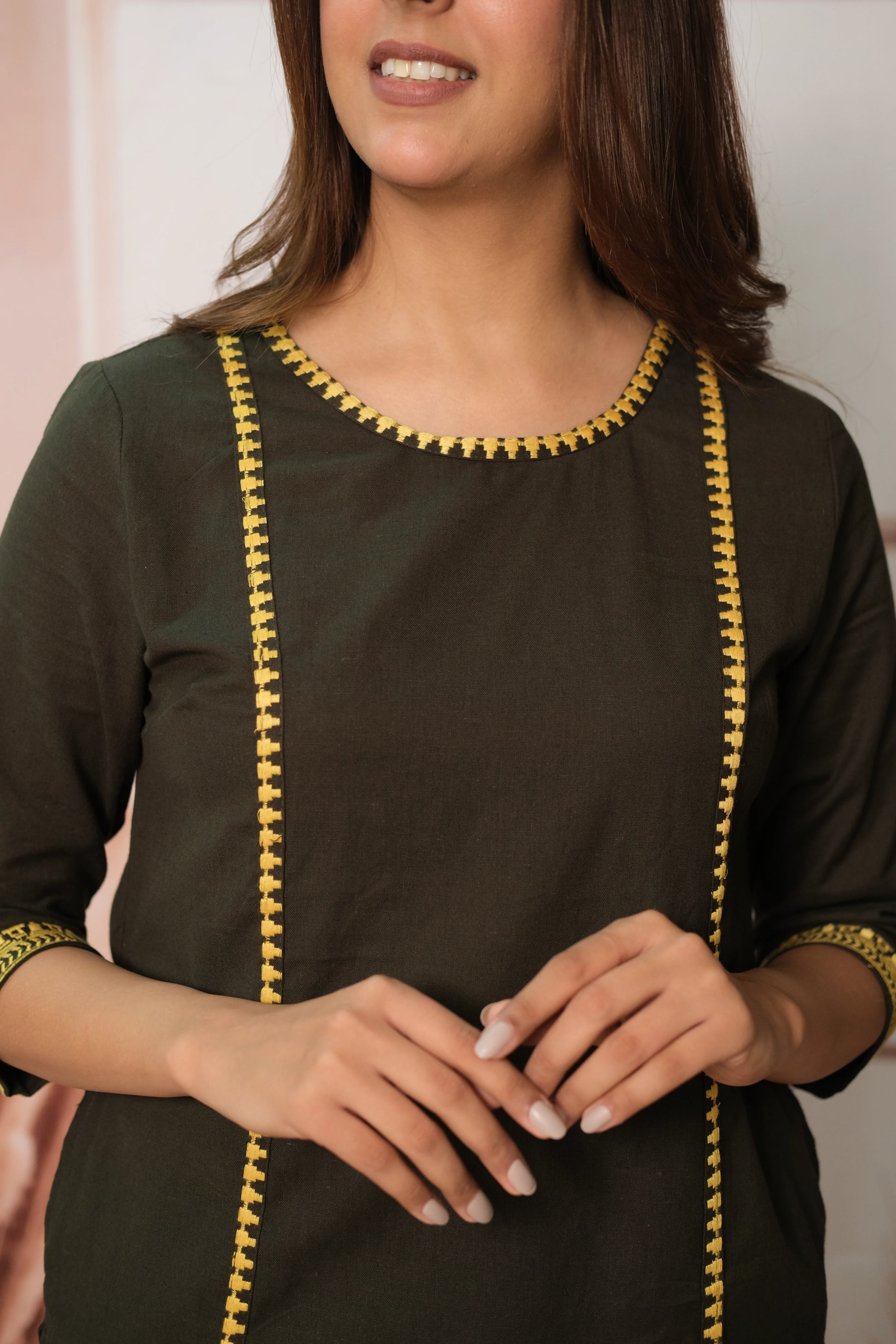 Woman wearing a black kurta with yellow embroidery, smiling.