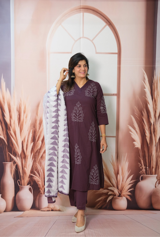 Woman in a purple outfit standing in front of a decorative wall with plants and vases.